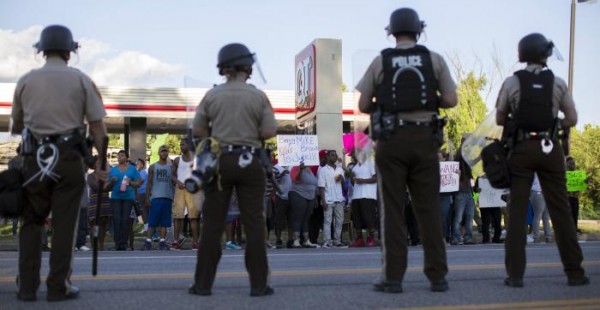 Police officers watch as demonstrators protest the death of black teenager Michael Brown in Ferguson
